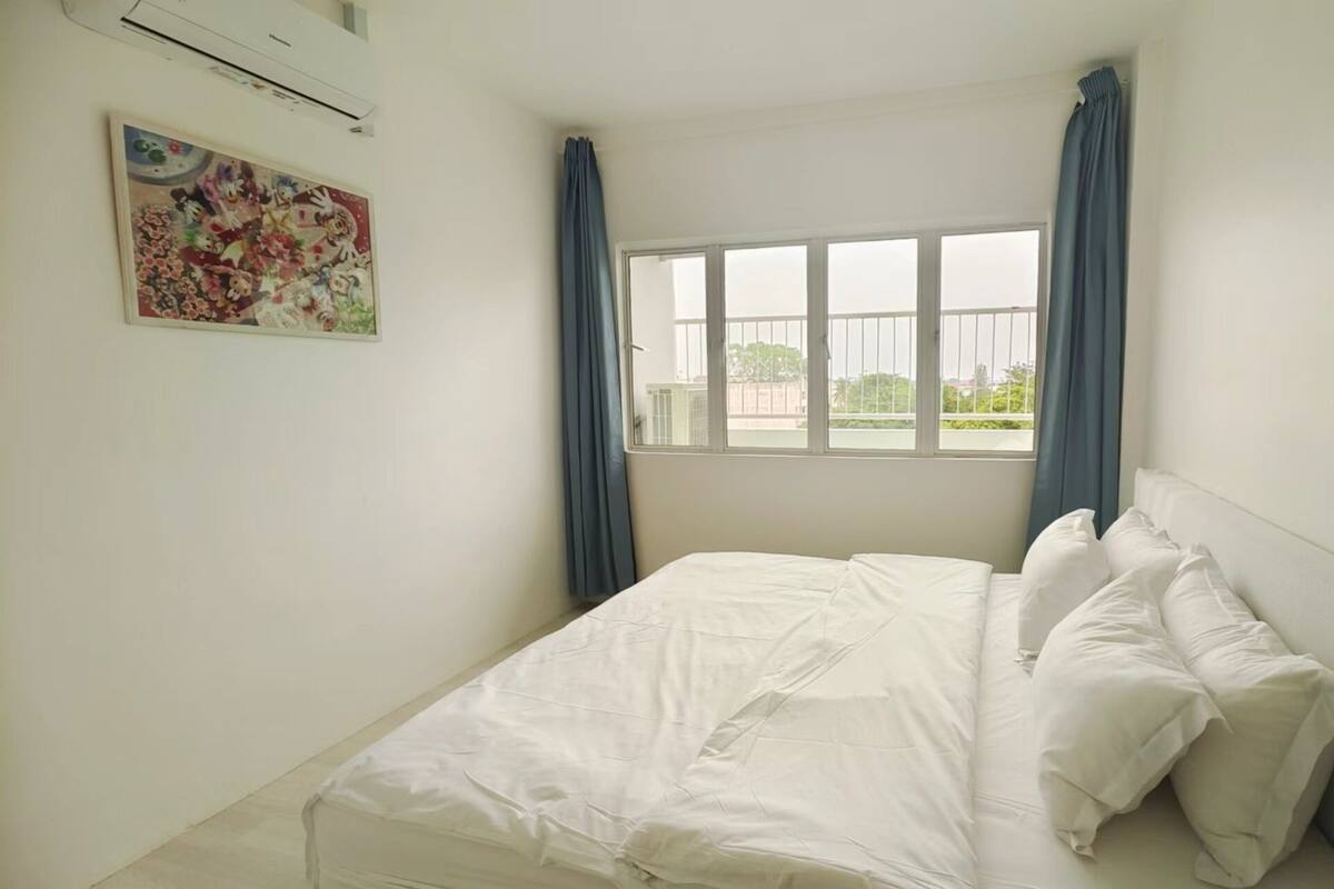 Een slaapkamer met een bed, een raam met gordijnen en een luchtverkoeler aan de muur.