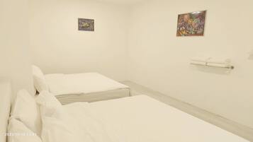 Ein schlicht eingerichtetes Hotelzimmer mit zwei Betten, einem kleinen Kunstwerk an der Wand und einem Handtuchhalter.