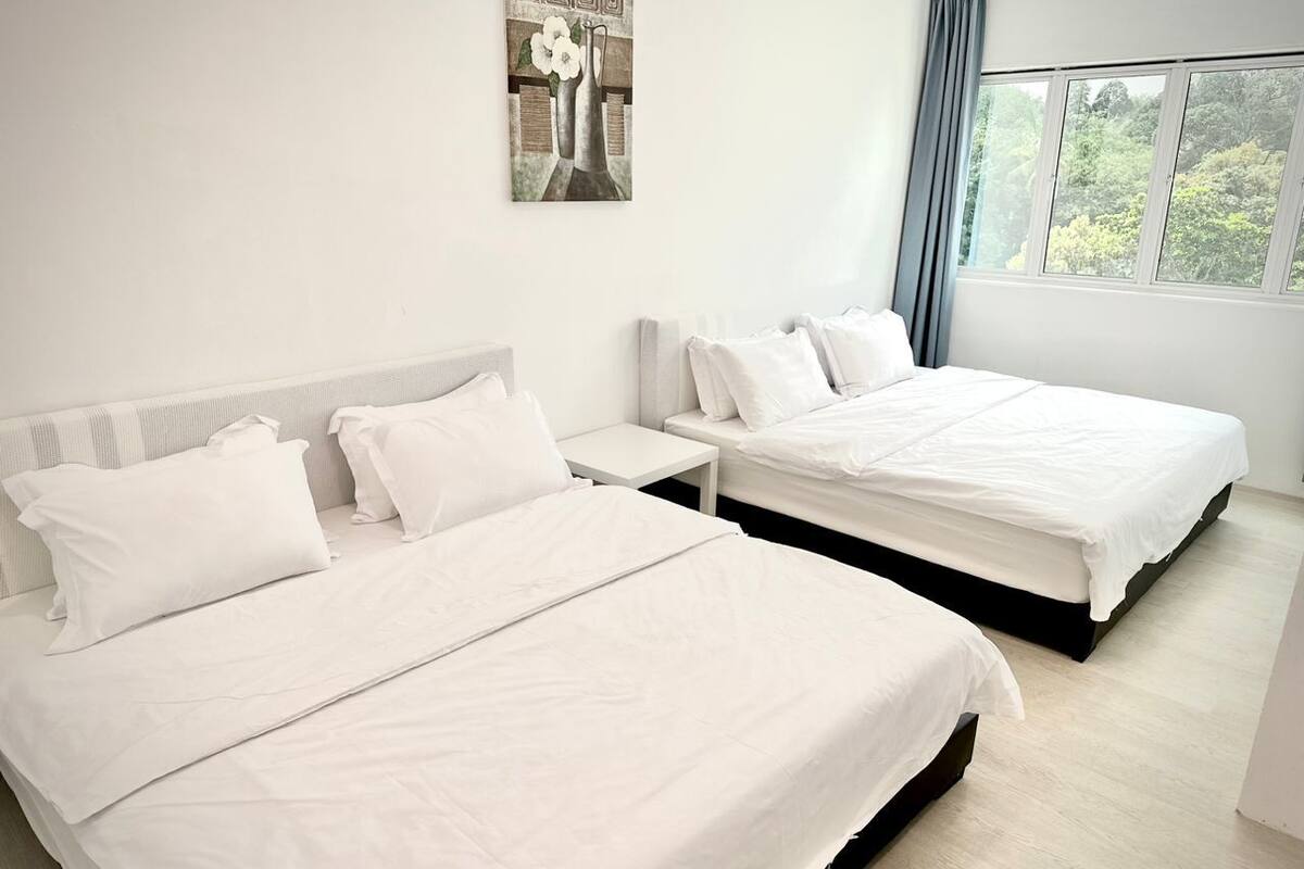 Een hotelkamer met twee bedden, een nachtkastje en een raam met uitzicht op bomen.