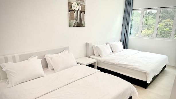 A hotel room with two beds, a nightstand, and a window with a view of trees.