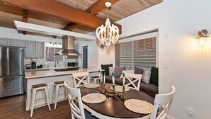 A modern kitchen with stainless steel appliances, a central island with bar stools, and a dining area with a round table and white chairs. - Revlands Cozy Cabin By Destination Big Bear: Close to Bear Mountain Ski Resort and Golf Course! Wood Burning Fireplace! Vaulted Ceilings! (Big Bear Lake)