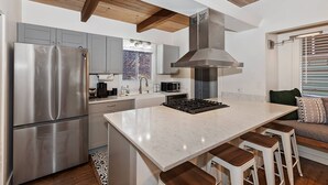 A modern kitchen with a stainless steel refrigerator, a built-in microwave, and a gas stove. There is a large island with bar stools and a window with blinds. - Revlands Cozy Cabin By Destination Big Bear: Close to Bear Mountain Ski Resort and Golf Course! Wood Burning Fireplace! Vaulted Ceilings! (Big Bear Lake)
