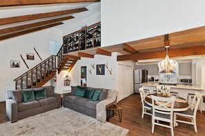 A spacious living area with a staircase, a dining area with a round table, and a kitchen with modern appliances.