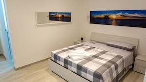 Een slaapkamer met een bed, nachtkastje, wandspiegel en twee landschapstekeningen.