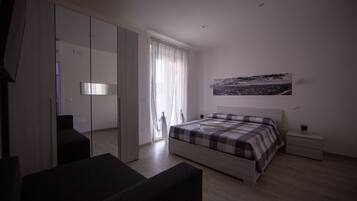 Un dormitorio con cama, mesita de noche, espejo y ventana con cortinas.