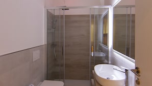 Een moderne badkamer met een glazen douchecabine, toilet, bidet en een wastafel met spiegel.
