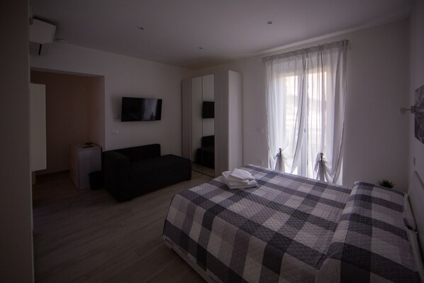 Un dormitorio con cama, sofá, televisión y ventana con cortinas.