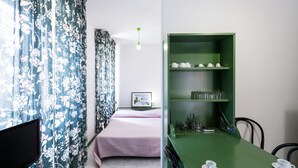 Ein Zimmer mit einem Bett, einem Fernseher, einem grünen Tisch mit Tassen und einem grünen Regal mit Tassen und Gläsern.