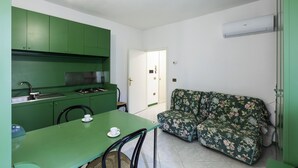 Eine kompakte Küche mit grünen Schränken, einem Esstisch mit zwei Stühlen und einem blumigen Sofa.