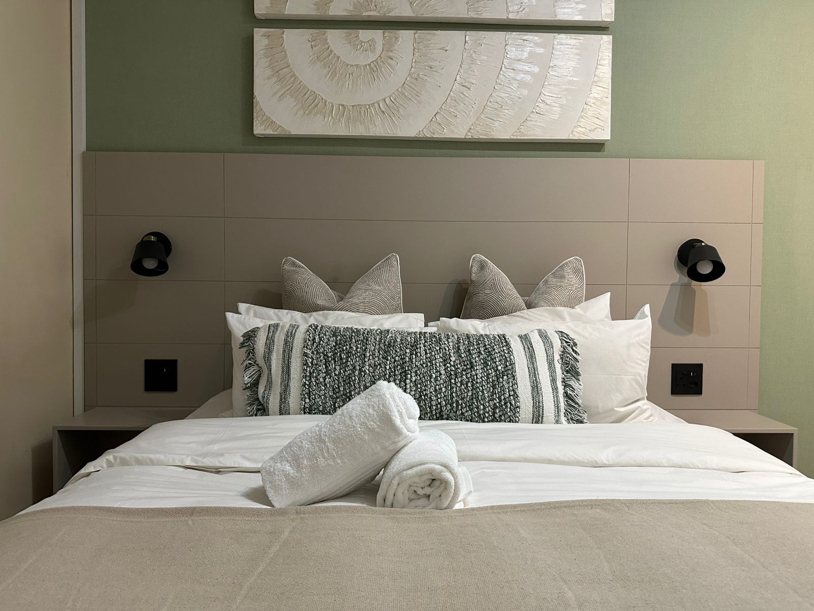 A neatly made bed with white linens, a rolled towel, and patterned pillows.