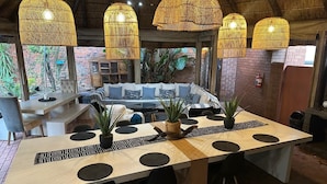 A dining area with a long table, black chairs, woven hanging lights, and potted plants. - Koi Liv-Inn (Germiston)