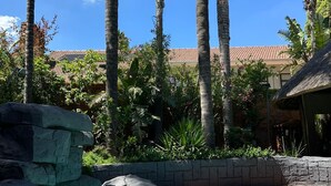 A swimming pool with clear blue water, surrounded by palm trees and a stone wall. - Koi Liv-Inn (Germiston)