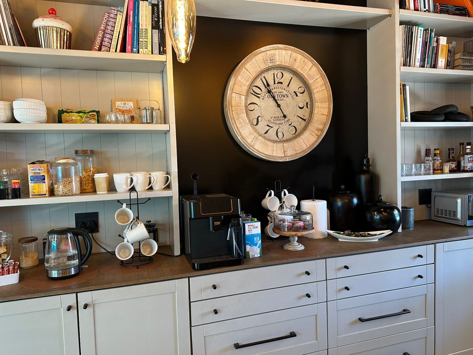 Eine Küche mit einer Vintage-Uhr, einer Kaffeemaschine und verschiedenen Küchenutensilien in Regalen.