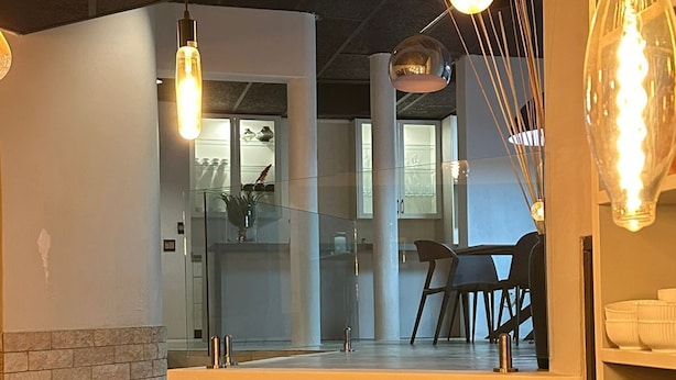 A modern interior with a dining area, a kitchen visible through a glass partition, and pendant lighting. - Koi Liv-Inn (Germiston)