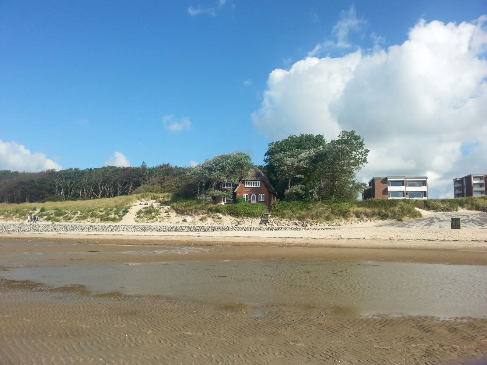 Ein Strand mit einem Haus und modernen Gebäuden im Hintergrund.