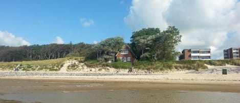 Una playa con una casa y edificios modernos al fondo.