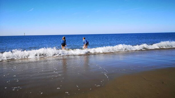 Una playa con dos personas caminando por la orilla.