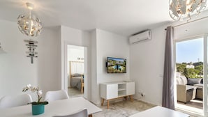 Habitació moderna i ben il·luminada amb zona de menjador, un llit amb cortina, televisió penjada a la paret i un balcó amb mobles d'exterior.