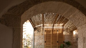 Zona esterna con sedute, pareti in pietra, porte in legno e tetto di paglia.