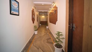 A hotel corridor with a sign indicating mask usage, potted plants, and a wooden door. - Hotel Ur (Prayagraj)