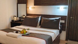 A neatly made bed with a tray of fruits and a glass of juice, a bedside table with a lamp, and a wooden headboard. - Hotel Ur (Prayagraj)