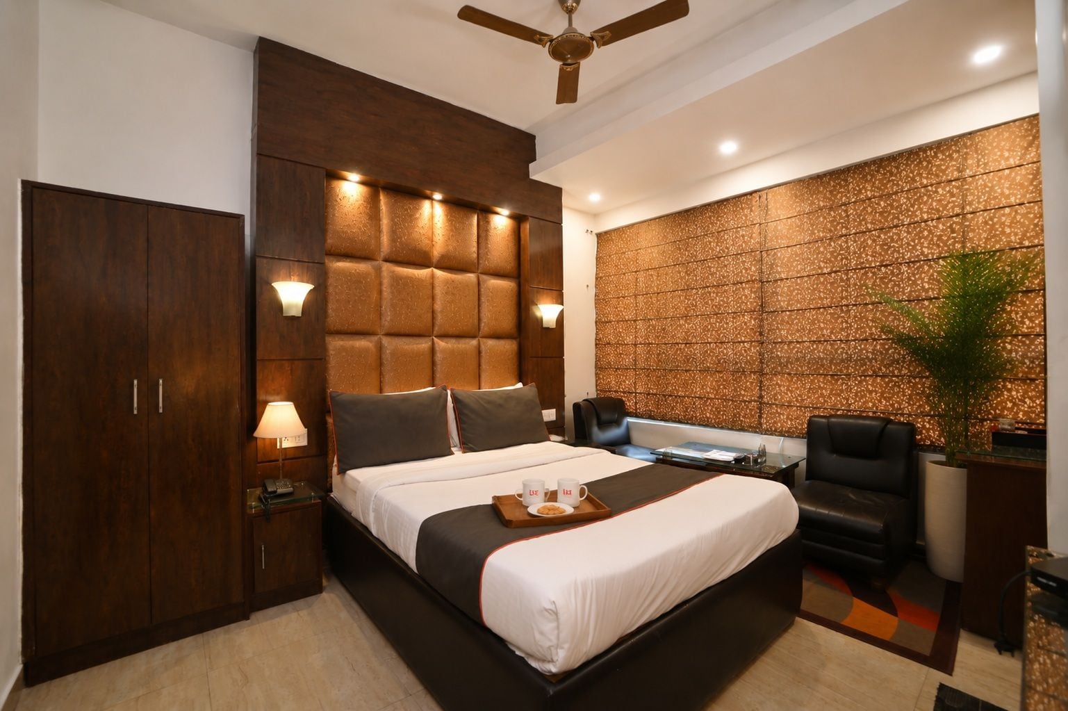 A modern hotel room with a large bed, a desk, a chair, a wardrobe, and a ceiling fan.
