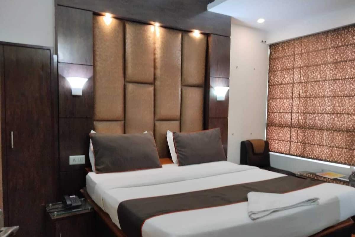 A hotel room with a large bed, a wardrobe, a bedside table, and a headboard with built-in lighting.