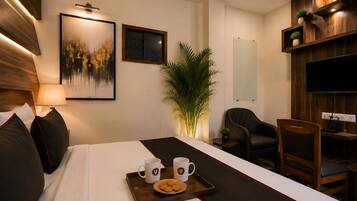 Una habitación de hotel con una cama, un escritorio, una silla, un televisor, una planta y obras de arte en la pared.