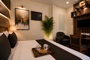 Una habitación de hotel con una cama, un escritorio, una silla, un televisor, una planta y obras de arte en la pared.