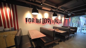 A restaurant interior with booths and tables, a wall with the text 'FOR THE LOVE OF PIZZA', and a view of the outside through a window.
