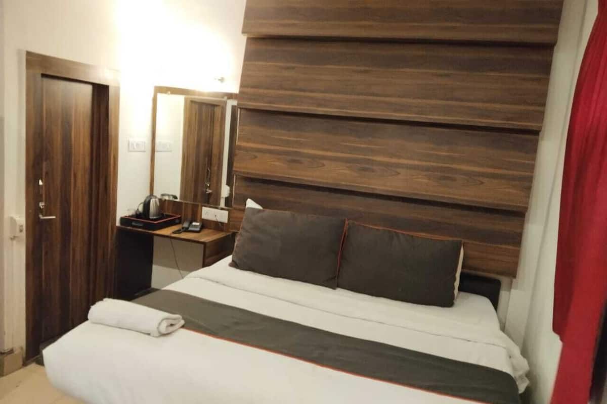 A hotel room with a bed, a bedside table with a lamp, a mirror, and a wooden headboard.