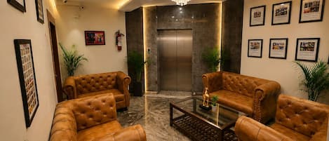 A modern lobby with leather sofas, a glass coffee table, a chandelier, and framed pictures on the walls.