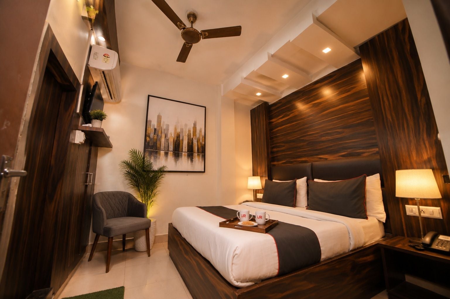 Una habitación de hotel con cama, mesita de noche, lámpara, silla y ventilador de techo.