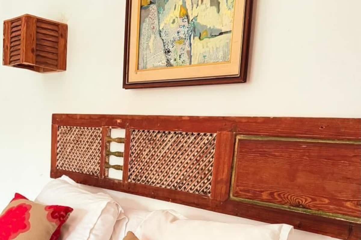 A bed with a wooden headboard, white and red floral bedding, and a framed painting above.