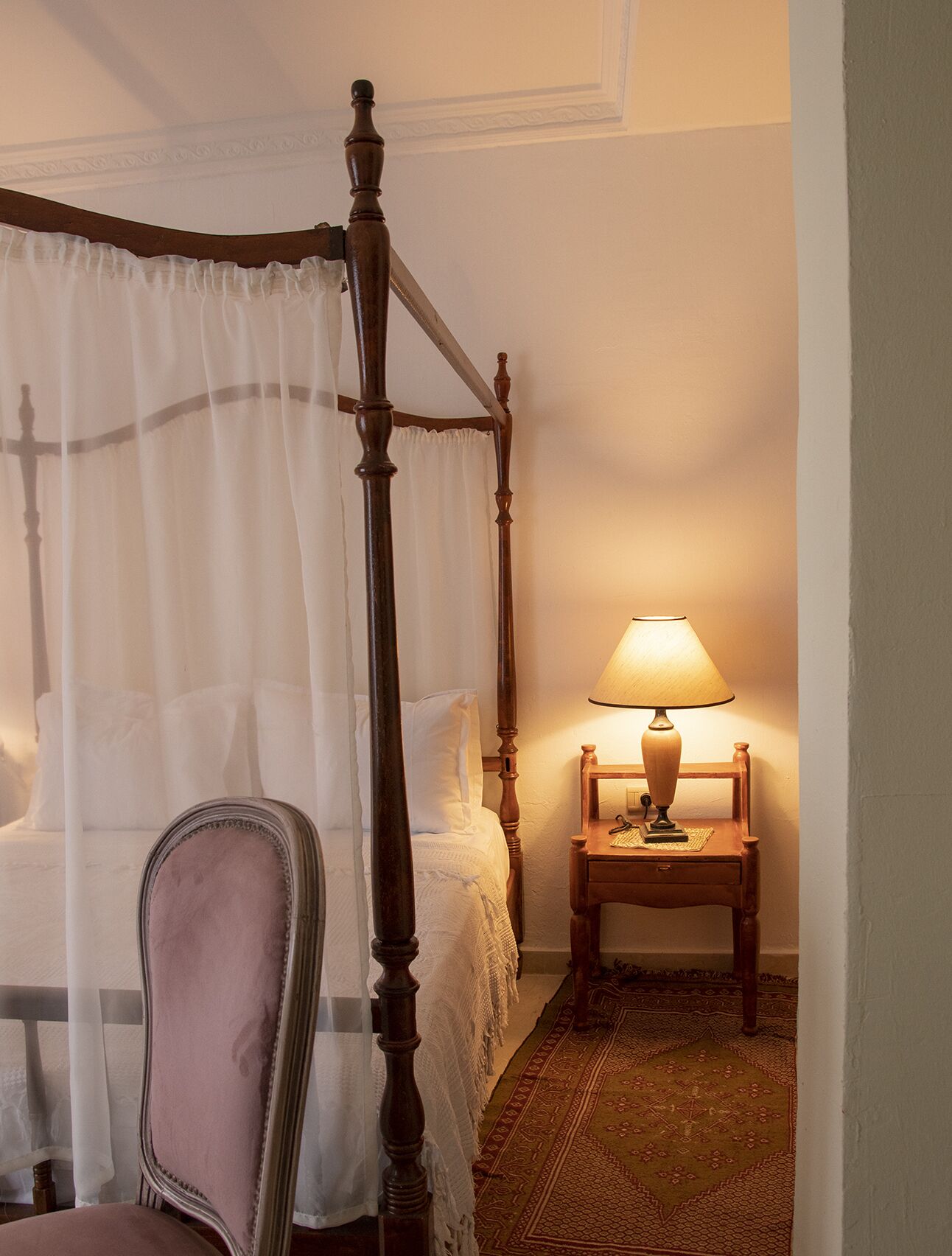 Een hemelbed, een nachtkastje met lamp en een stoel.