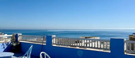 A terrace with a view of the sea, featuring a round table, two chairs, and a railing.