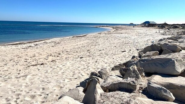 A beach with clear skies, a sandy shore, and large rocks in the foreground. - dar Yessine (Hergla)