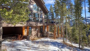 A modern cabin with a glass balcony, surrounded by snow-covered trees and a clear sky.