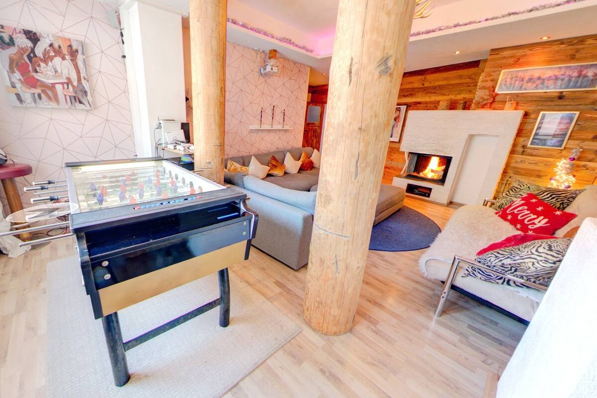 A cozy living room with a foosball table, a fireplace, and a sofa with festive pillows.