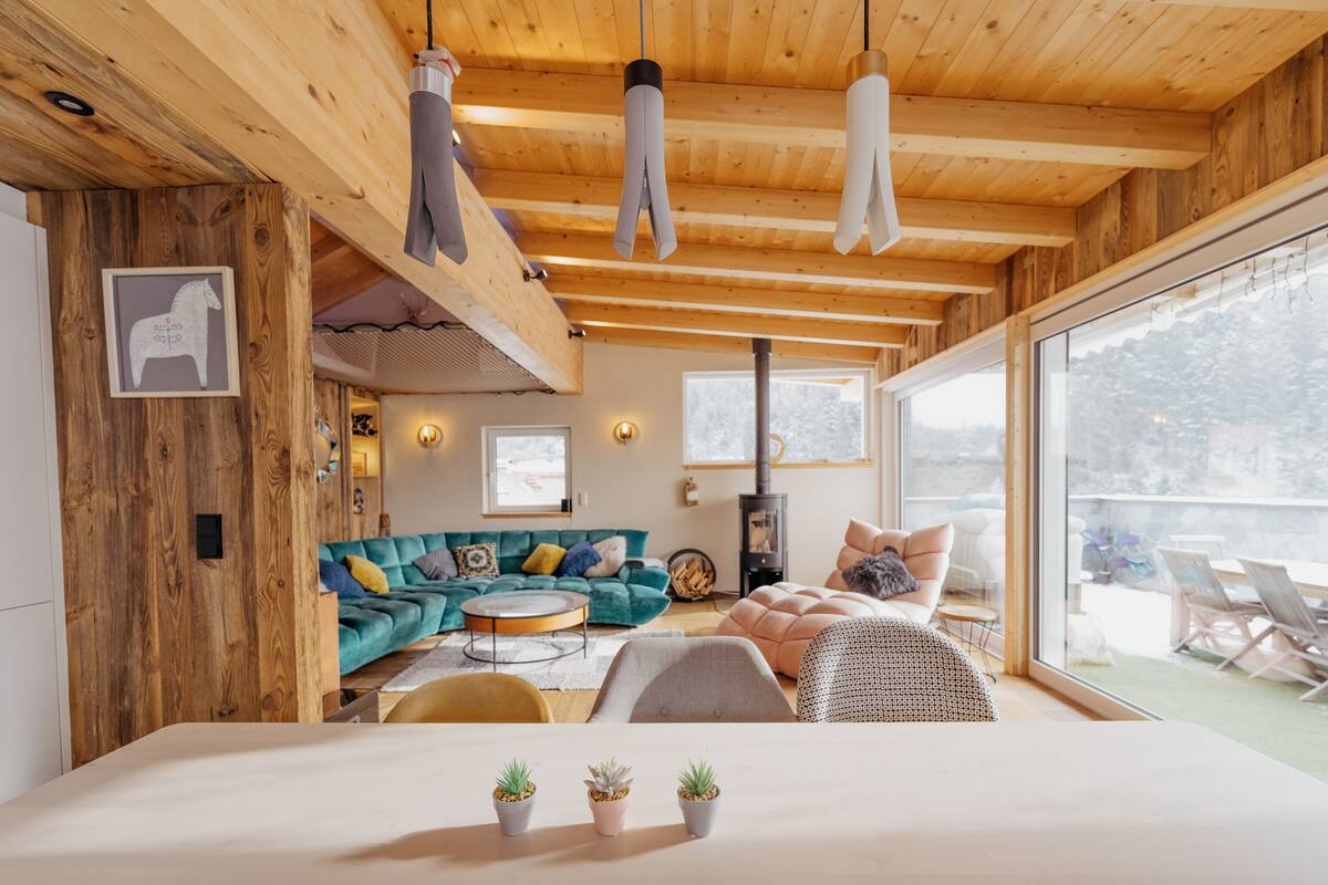 A modern interior with wooden beams, a sofa, a bed, and a view through large windows.