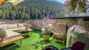 A patio with a sofa, chairs, and a grill area, overlooking a forested mountain. - Doug's Mountain Getaway (Fulpmes)