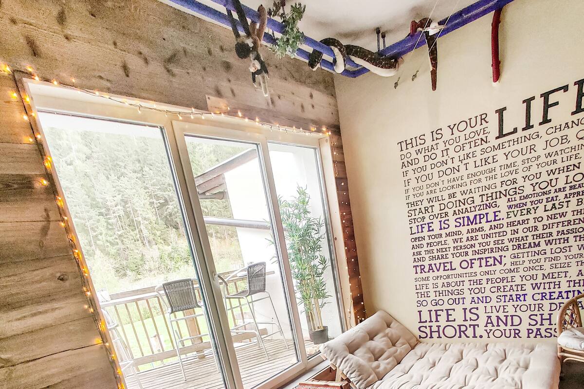 A cozy room with a large window, a comfortable seating area with cushions, and a wall with inspirational text.