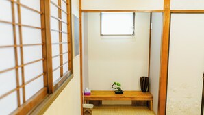 Una habitación japonesa tradicional con suelo de tatami, puerta corredera shoji, una ventana pequeña, un banco de madera y una planta en maceta.