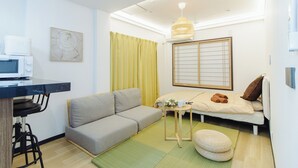 Un espacio habitable compacto con un sofá, una mesita con una taza y toallas, un microondas y una tradicional pantalla japonesa shoji.
