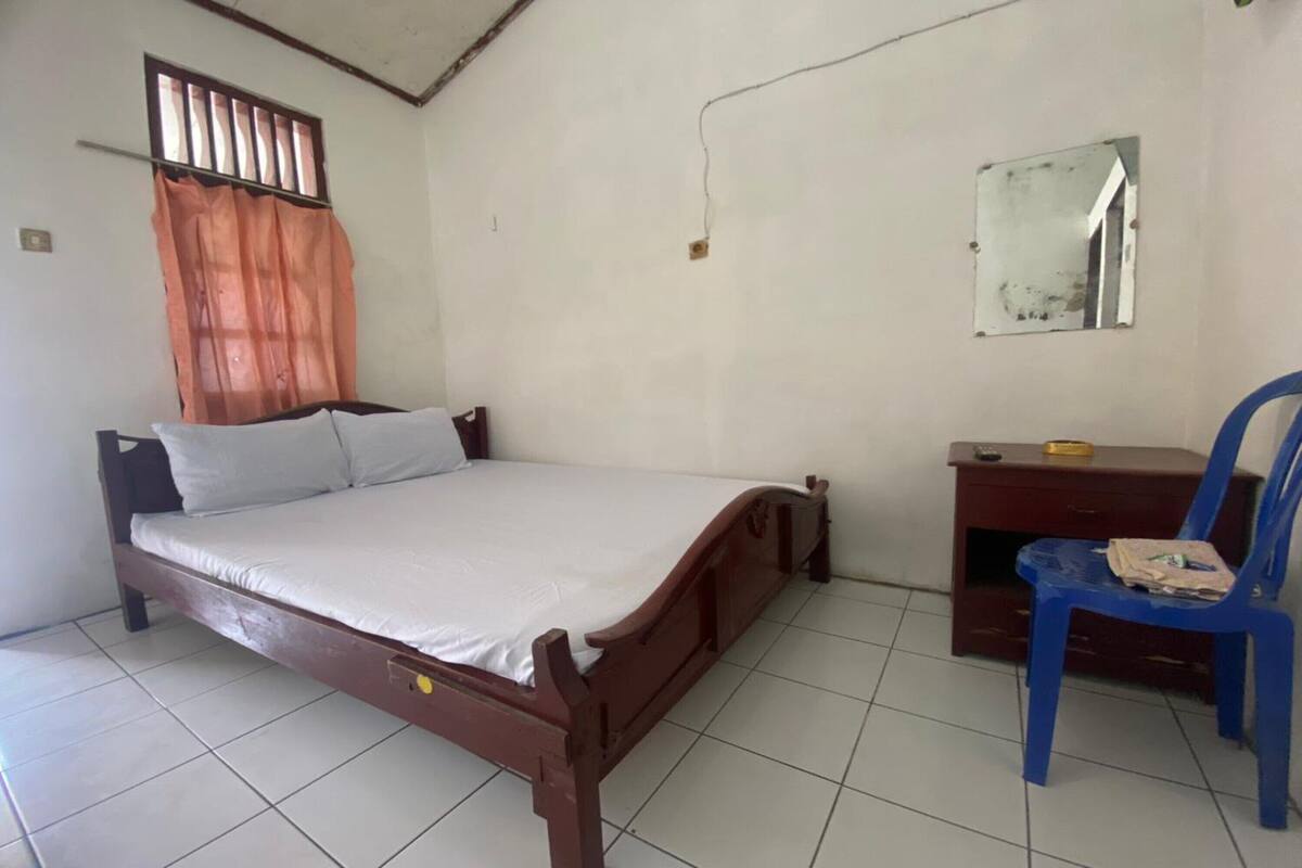 A bedroom with a wooden bed, a desk with a chair, a mirror, and a window with curtains.