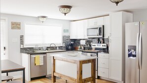 A modern kitchen with white cabinets, a wooden island, stainless steel appliances, and a window with blinds.