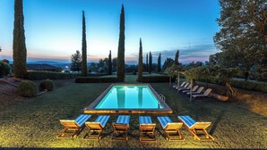 A swimming pool with six sun loungers in a garden setting.