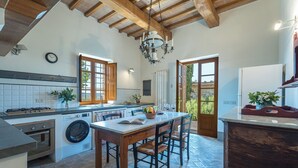 A kitchen with a central island, wooden beams, a chandelier, and a view through the door.