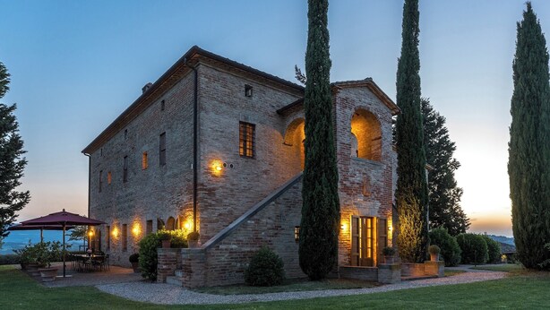 A stone building with a patio area, large windows, and tall trees.