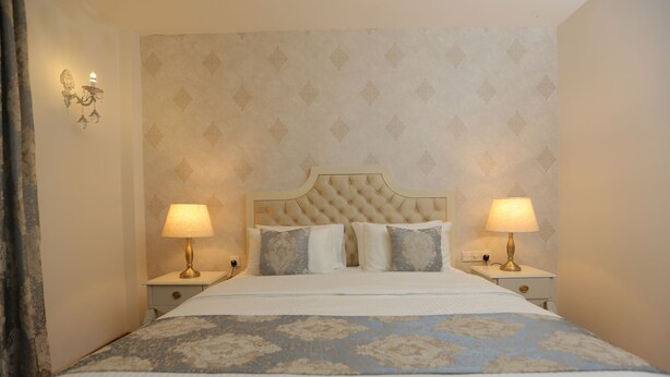 A neatly made bed with a floral bedspread, two bedside lamps, and a patterned wallpaper. - Nicholas Cottage (Labukele)